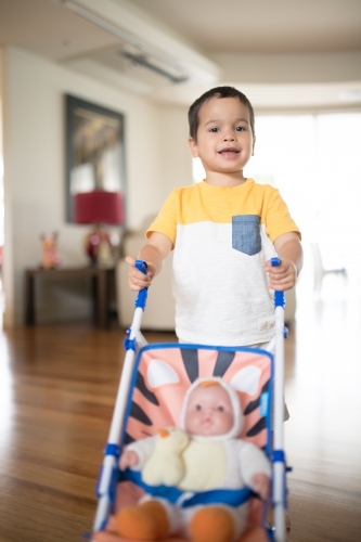 Two year old boy pushing toy stroller with a doll - Australian Stock Image