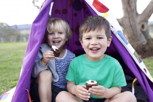 Two young boys eating cupcakes in a tent smiling - Australian Stock Image