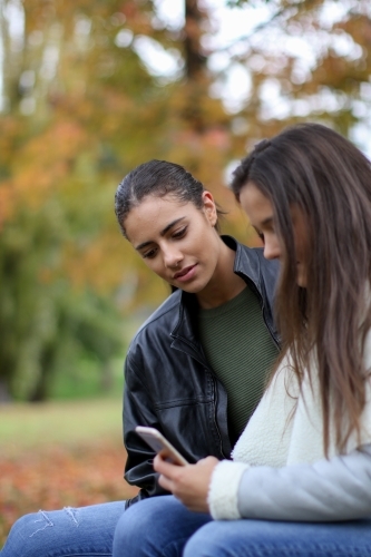 Two young female friends sitting together in an outdoor setting - Australian Stock Image