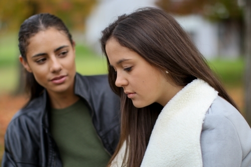 Two young female friends sitting together in an outdoor setting - Australian Stock Image