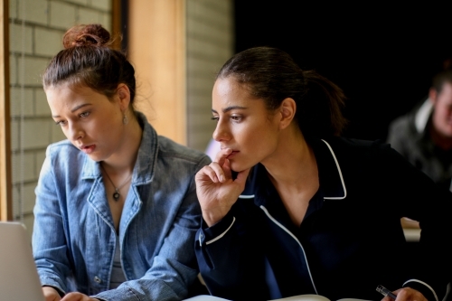 Two young females sitting at a desk in a classroom looking at a computer - Australian Stock Image