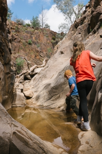 Two young kids climbing around a water filled canyon on a bush walk