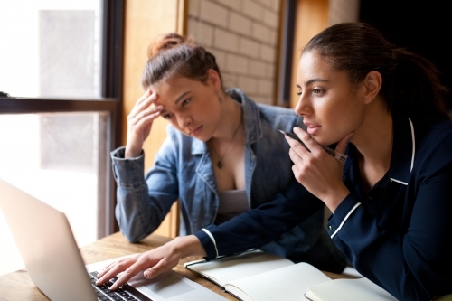 Two young women sitting at a desk in a classroom