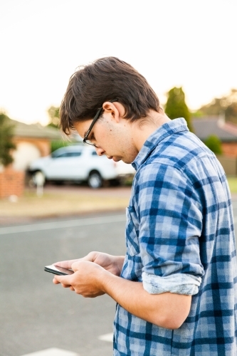 Uni student waiting at bus stop using mobile phone - Australian Stock Image
