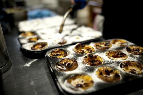 Using blow torch to caramelise freshly made Portugese tarts in tin at bakery cafe - Australian Stock Image