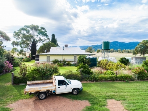 Ute parked outside of farmhouse on rural country property in morning light seen from aerial view - Australian Stock Image