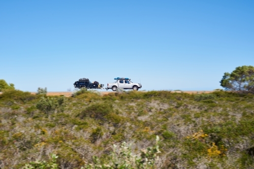 Ute towing a camper trailer on a road trip in coastal Western Australia, with motion blur.