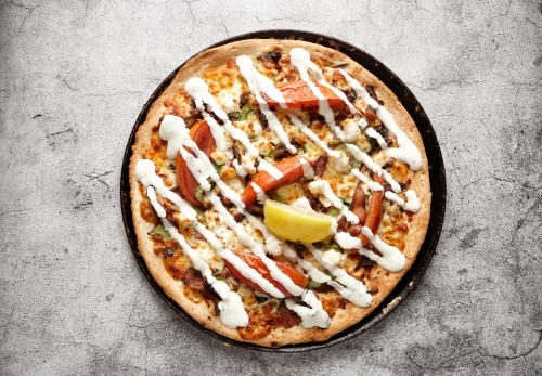 Vegetarian supreme pizza drizzled with white sauce and topped with a lemon slice - Australian Stock Image