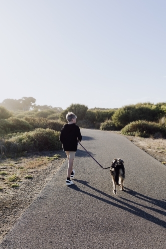 Vertical image of boy walking dog along walking path at sunset - Australian Stock Image