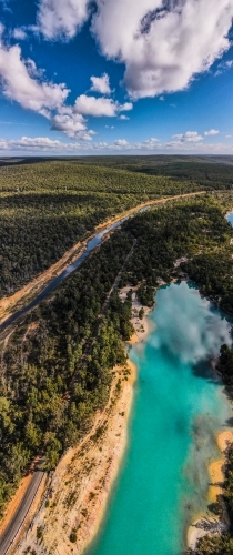 vertical shot of a blue lake surrounded with green trees on a sunny day with white and blue skies - Australian Stock Image