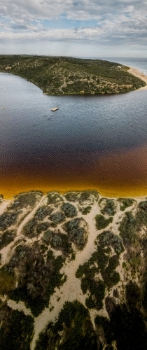 vertical shot of an island with boat floating, bushes, yellow sand on a sunny day - Australian Stock Image