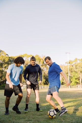 vertical shot of men playing soccer in the field on a sunny day with clear skies - Australian Stock Image