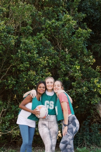 vertical shot of three young smiling women in sports clothes with one holding a net ball - Australian Stock Image