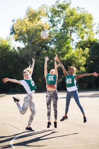 vertical shot of three young women jumping in mid air with one trying to catch a ball on a sunny day - Australian Stock Image