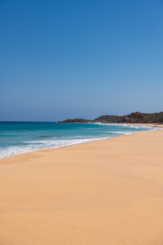 Vertical view looking along sandy beach with waves towards a headland - Australian Stock Image