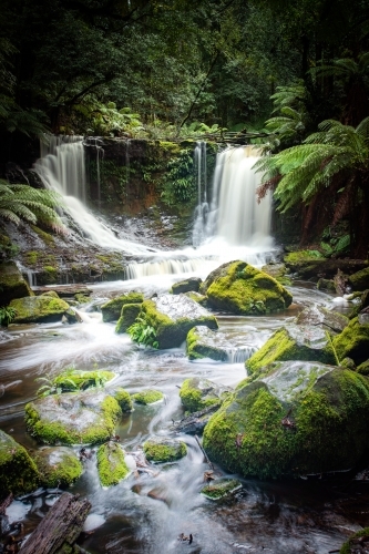 Vertical view of Green moss covered stones in front of a flowing waterfall. - Australian Stock Image