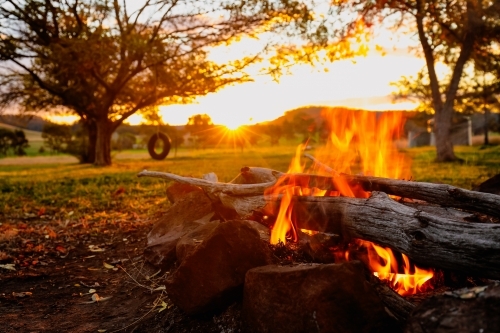 Vibrant orange campfire at sunset with tyre swing hanging from tree in background - Australian Stock Image