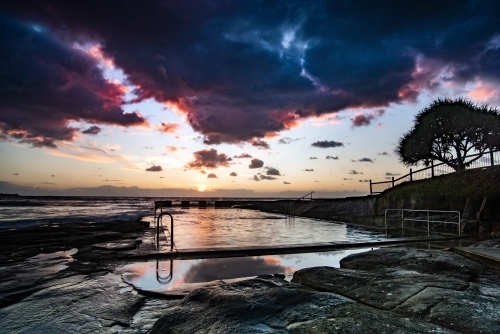 Vibrant sunrise colours in the sky over the ocean pool - Australian Stock Image