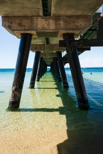 View between pylons under a jetty to the horizon with clear water - Australian Stock Image