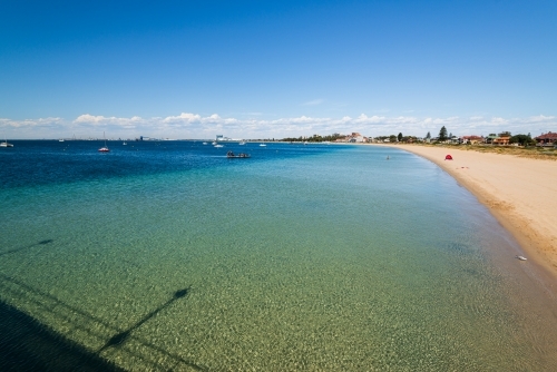 View from jetty of sandy beach, clear green blue water and swimming platform with people