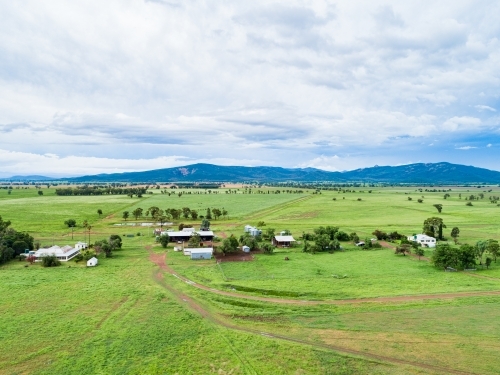 View of distant farm home area with house and sheds among green paddocks - Australian Stock Image