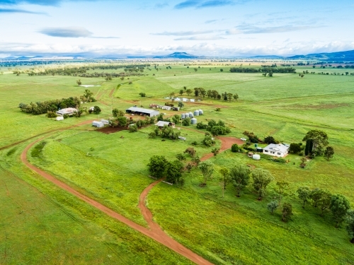 View of distant farm home area with house and sheds among green paddocks - Australian Stock Image