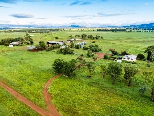 View of distant farm home area with house and sheds among green paddocks - Australian Stock Image