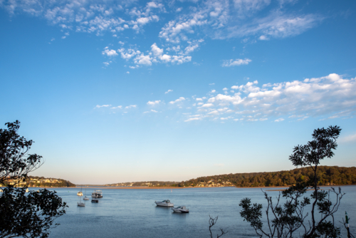 View of the Hacking River near sunset with boats on the water and clouds in the sky - Australian Stock Image