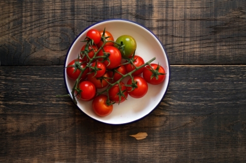 Vine ripened tomatoes in white enamel dish on black wooden background - Australian Stock Image