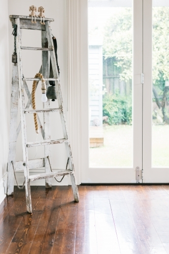 Vintage decor collection of an old ladder, farm bell and rope light in a contemporary home - Australian Stock Image