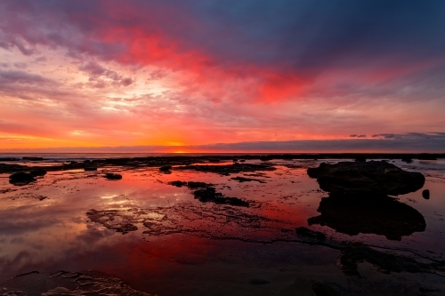 Vivid reflections of sunrise on coastal seascape at low tide - Australian Stock Image