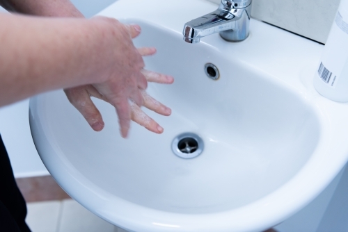 Washing hands with soap and water at basin - Australian Stock Image