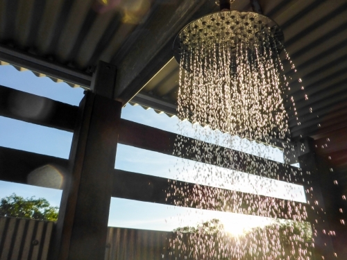 Water flowing from a showerhead with sunbeam filtering through - Australian Stock Image