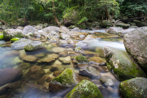 Water of the Mossman River flows over ancient rocks and boulders in Mossman Gorge, Queensland - Australian Stock Image