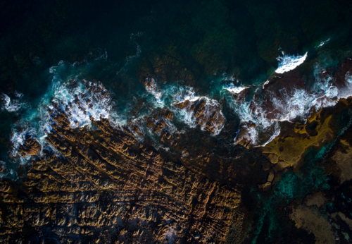 Waves collapse gently on jagged rock. - Australian Stock Image