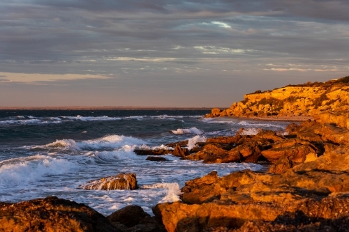 waves crashing on rocks in late afternoon light - Australian Stock Image