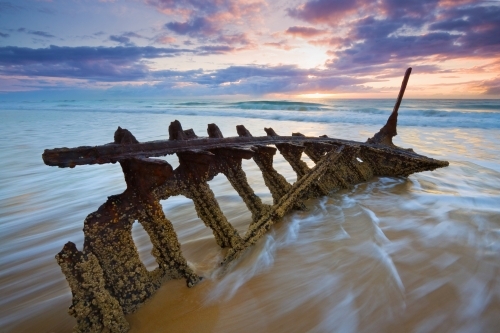 Waves engulfing the bow of a shipwreck on a beach - Australian Stock Image