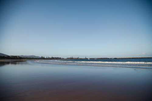 Waves rolling in on Coffs Harbour Beach with jetty in the distance, NSW Australia - Australian Stock Image