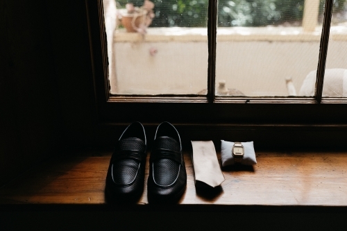 Wedding accessories for husband lined up on window sill shoes tie and watch - Australian Stock Image