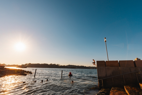 Wet kids jumping from ledge into water at Marrinawi Cove in bright afternoon sunshine - Australian Stock Image