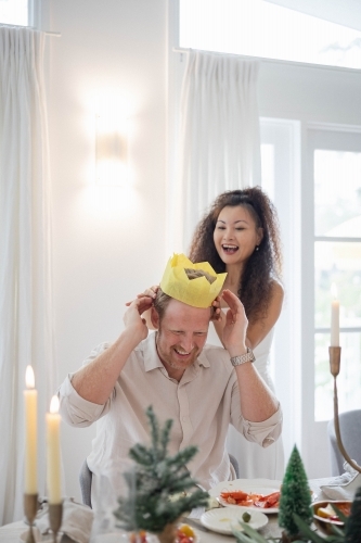 Wife and husband wearing Christmas crown at dining table - Australian Stock Image