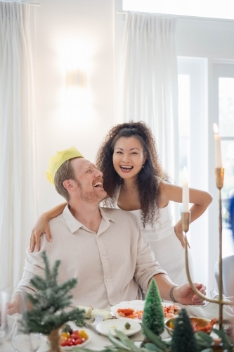 Wife and husband wearing Christmas crown at dining table - Australian Stock Image