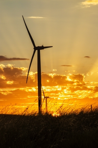 Wind turbine silhouette against sunset with rays - Australian Stock Image