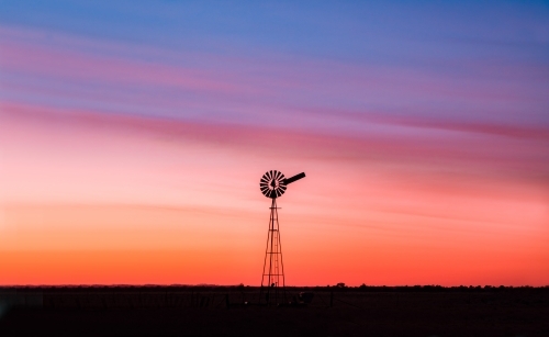 Windmill at dawn with the coloured sky in a clear setting - Australian Stock Image