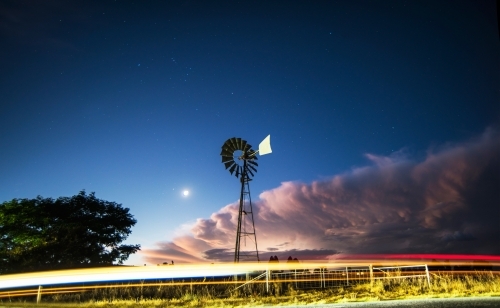 Windmill silhouette in the night as a storm approaches and a car lights go past - Australian Stock Image