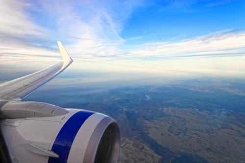 Wing and engine of aeroplane with blue sky and earth below - copy space - Australian Stock Image