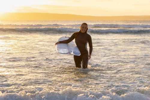 woman carrying surfboard out of the ocean - Australian Stock Image