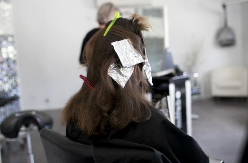 Woman from behind sitting with foils in her hair at hairdressers - Australian Stock Image