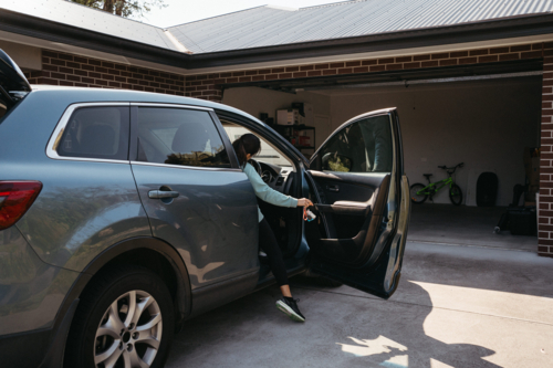 Woman getting out of the driver seat of the car outside home - Australian Stock Image