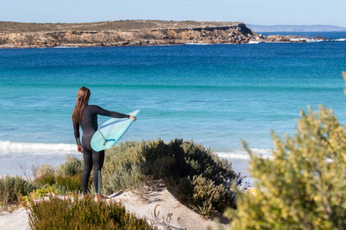 Woman holding surfboard with view of coastline and blue water in South Australia - Australian Stock Image